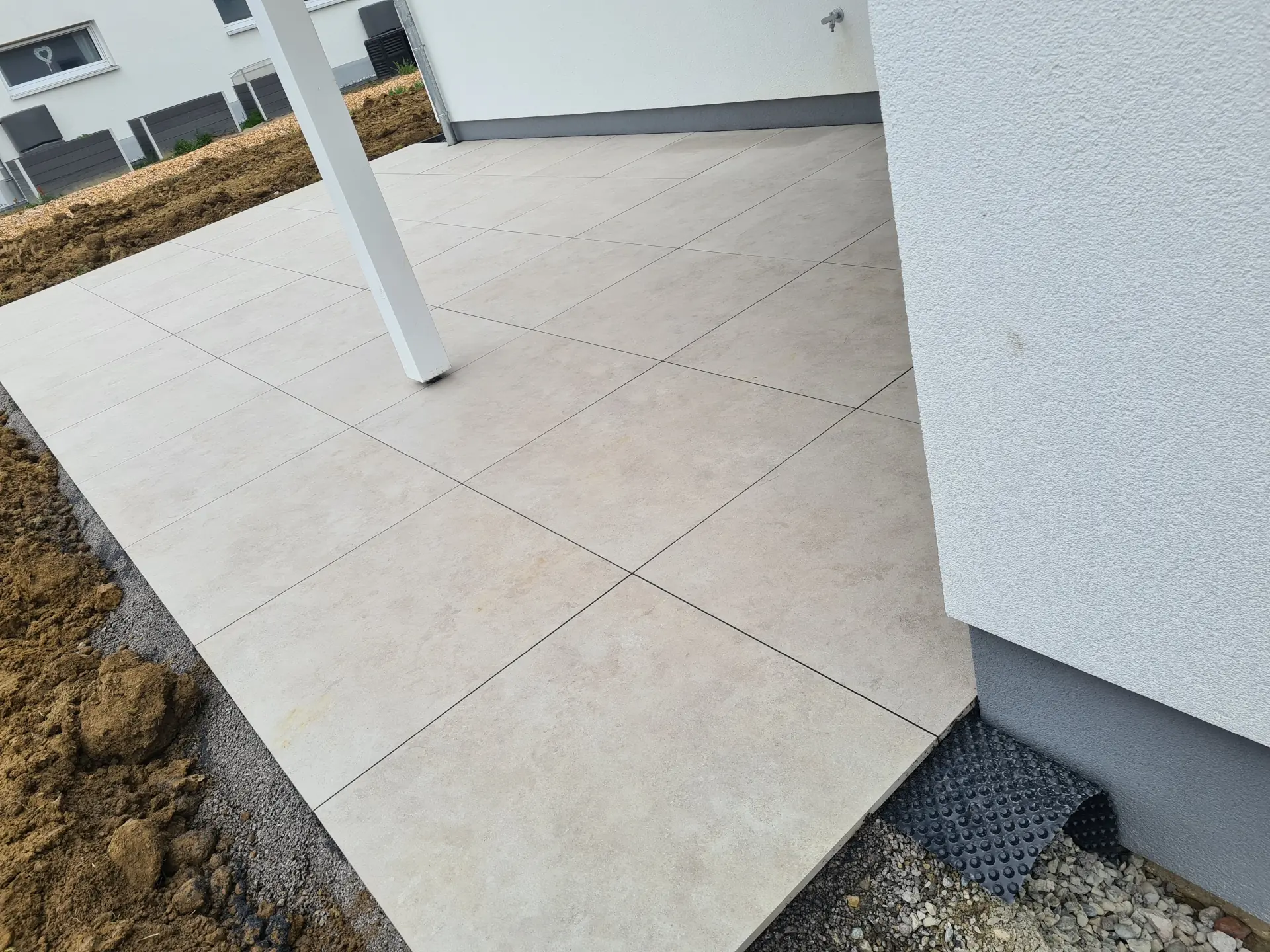 Moderne Lounge-Terrasse mit beigem Terrassenbelag als gemütlicher Sitzbereich im Garten
